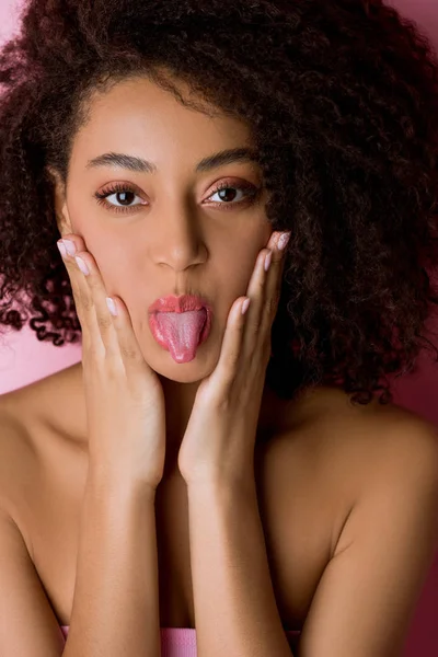 Portrait of happy curly african american girl sticking tongue out on pink — Stock Photo