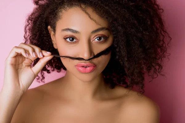 Portrait of funny african american girl making fake mustache from hair on pink — Stock Photo