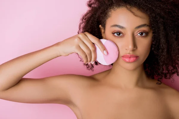 Mulher americana africana nua com olhos fechados usando escova facial de limpeza de silicone, isolada em rosa — Fotografia de Stock