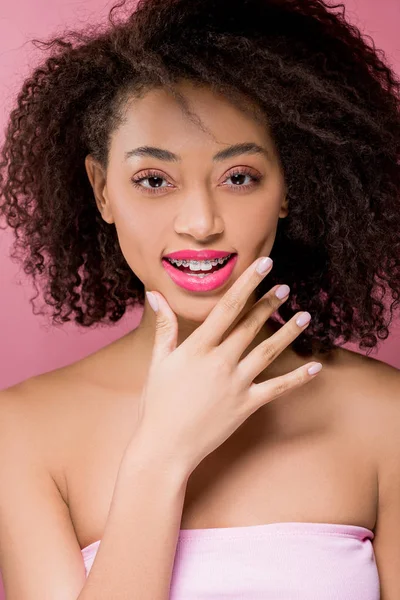 Feliz rizado chica afroamericana con frenos dentales, aislado en rosa - foto de stock