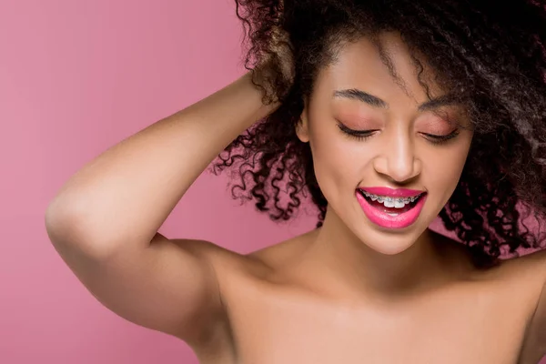 Alegre encaracolado nua menina americana africana com aparelho dentário, isolado em rosa — Fotografia de Stock