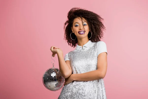 Happy emotional african american girl in paillettes dress holding disco ball, isolated on pink — Stock Photo