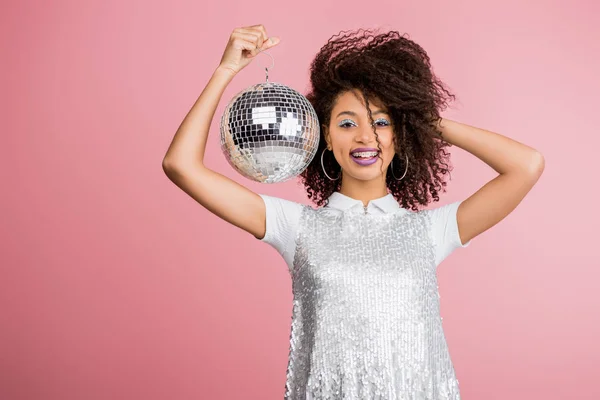 Sorridente menina afro-americana em paillettes vestido segurando bola de discoteca, isolado em rosa — Fotografia de Stock