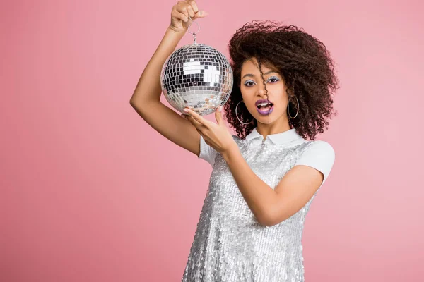 Shocked african american girl in paillettes dress holding disco ball, isolated on pink — Stock Photo