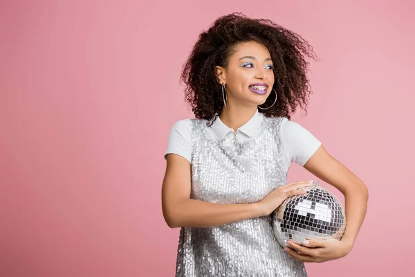 Bella sorridente ragazza afroamericana in abito paillettes tenendo palla disco, isolato su rosa — Foto stock