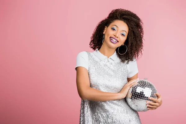 Красивая улыбающаяся африканская американка в платье из пайетки, держащая диско-мяч, изолированный на розовом — стоковое фото