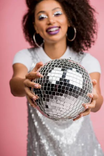 Selective focus of happy african american girl in paillettes dress holding disco ball, isolated on pink — Stock Photo