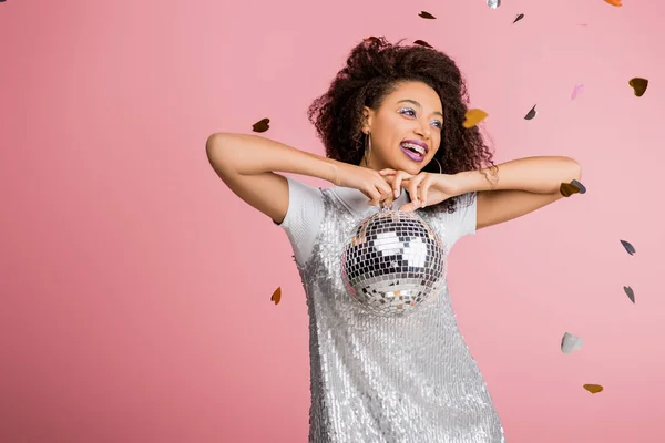 Menina americana africana feliz em paillettes vestido segurando bola de discoteca, isolado em rosa com confete — Fotografia de Stock