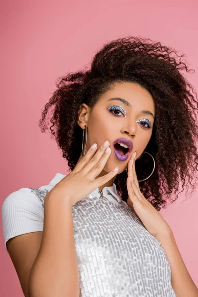 Shocked african american girl with silver glitter eyeshadows and purple lips wearing paillettes dress, isolated on pink — Stock Photo