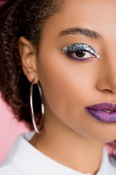 Chica afroamericana con sombras de ojos de brillo plateado y labios morados, aislado en rosa - foto de stock