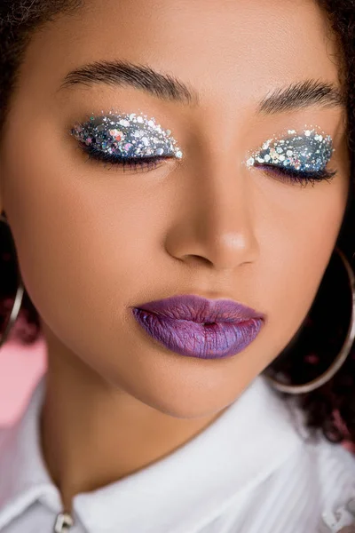 Ragazza afroamericana con ombretti scintillanti d'argento su occhi chiusi e labbra viola, isolate su rosa — Foto stock