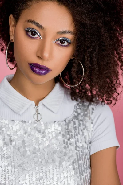 Chica afroamericana con sombras de ojos de brillo plateado y labios púrpura usando paillettes vestido, aislado en rosa - foto de stock