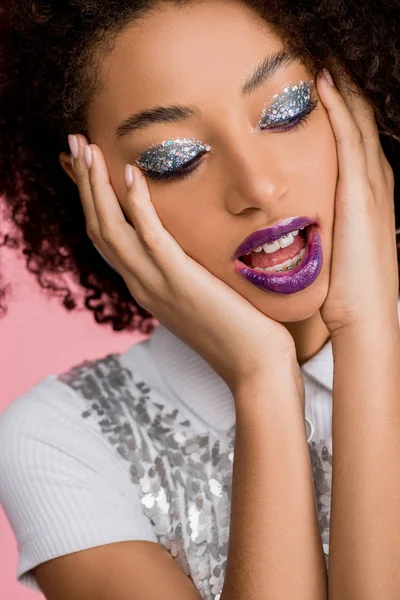 Chica afro-americana emocional con sombras de ojos de brillo plateado y labios morados usando paillettes vestido, aislado en rosa - foto de stock