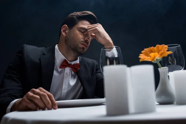 Enfoque selectivo del hombre cansado sentado en la mesa servida aislado en negro - foto de stock