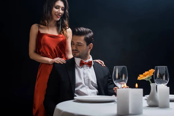 Beautiful smiling woman standing beside handsome man in suit at served table isolated on black — Stock Photo