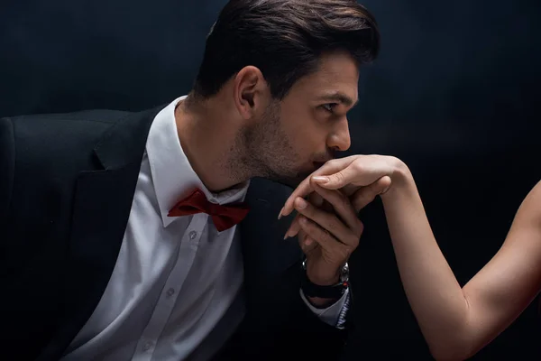 Handsome man in suit kissing hand of woman isolated on black — Stock Photo