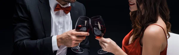 Panoramic shot of elegance couple clinking with wine glasses isolated on black — Stock Photo