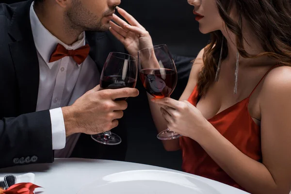 Vista cortada de brinde casal elegante com vinho durante o jantar romântico isolado em preto — Fotografia de Stock
