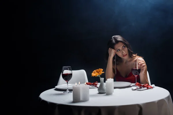 Mulher bonita com mão pela cabeça olhando para a mesa servida no fundo preto com fumaça — Fotografia de Stock