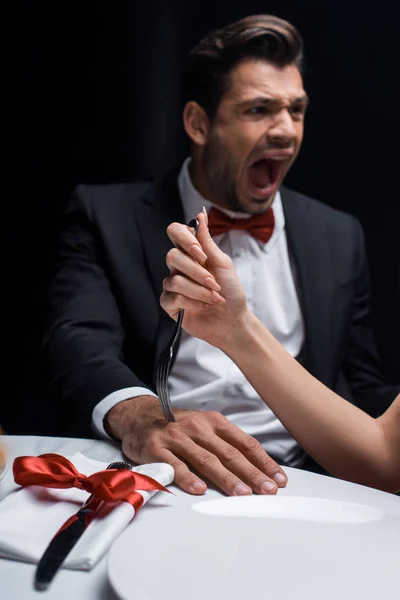 Foyer sélectif de femme collant fourchette dans la main de petit ami hurlant pendant le dîner romantique isolé sur noir — Photo de stock