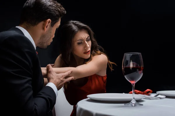 Enfoque selectivo de pareja peleando por copa de vino en mesa servida aislada en negro - foto de stock