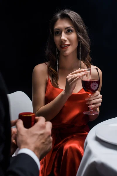 Concentration sélective de la femme élégante avec verre à vin en regardant petit ami avec boîte à bijoux isolé sur noir — Photo de stock