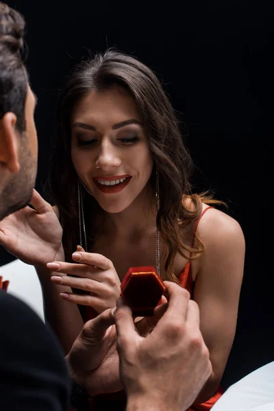 Focus selettivo dell'uomo che presenta portagioie alla fidanzata sorridente a tavola isolata sul nero — Foto stock