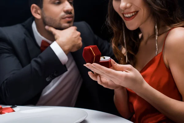 Foyer sélectif de souriante femme tenant bague de bijoux dans la boîte par beau petit ami à la table servie isolé sur noir — Photo de stock