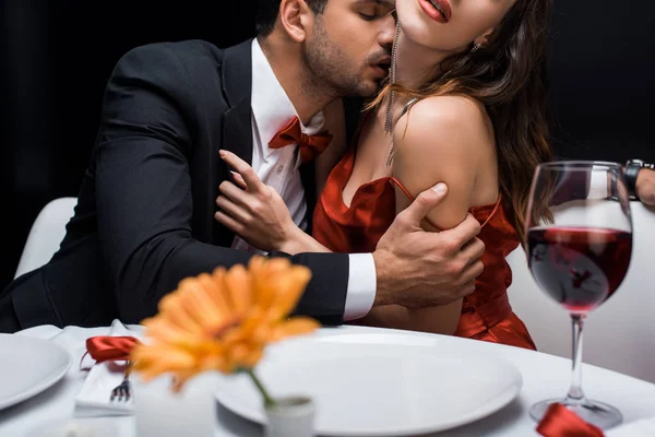 Focus selettivo di uomo elegante baciare in donna collo al tavolo servito isolato su nero — Foto stock