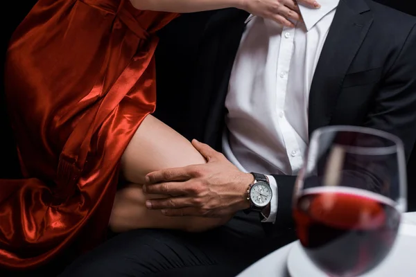 Обрізаний вид чоловіка, що тримається на коліні елегантної жінки під час романтичної вечері ізольовано на чорному — стокове фото