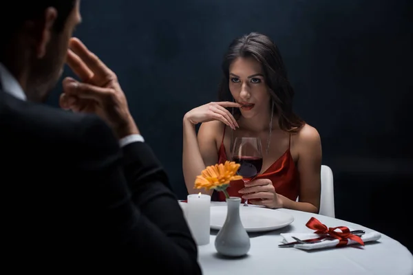 Selective focus of seductive woman with finger by lips looking at man during romantic dinner isolated on black — Stock Photo
