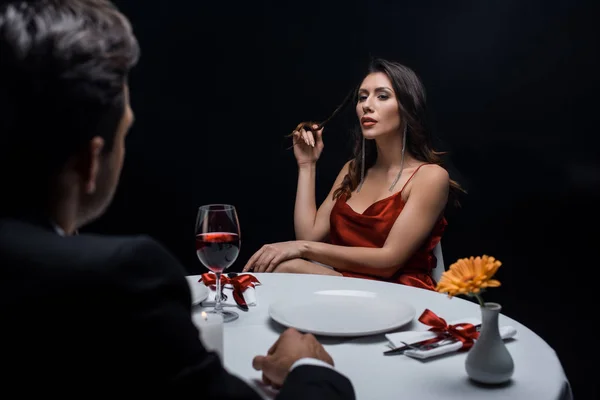 Enfoque selectivo de la mujer elegante mirando al hombre durante la cena romántica aislado en negro - foto de stock