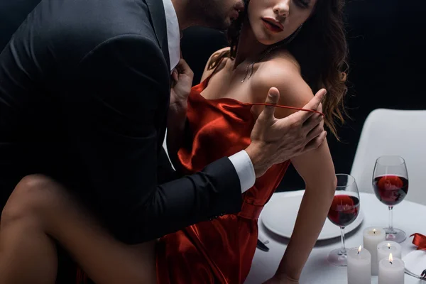 Cropped view of elegant man taking off dress of woman during romantic dinner isolated on black — Stock Photo