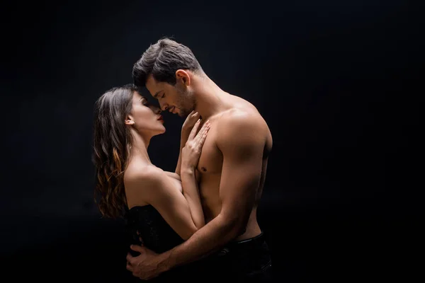 Side view of handsome shirtless man hugging beautiful woman isolated on black — Stock Photo