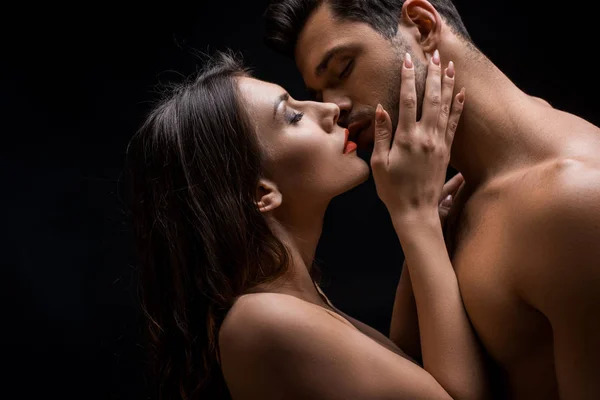 Side view of beautiful naked woman kissing shirtless man isolated on black — Stock Photo