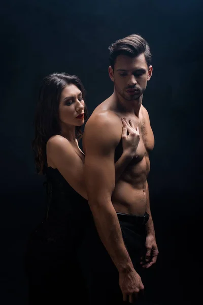 Side view of attractive girl touching shirtless man isolated on black — Stock Photo