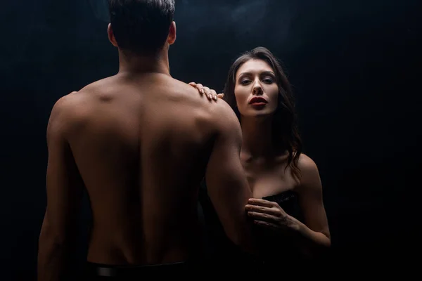 Sexy woman standing by muscular boyfriend and looking at camera isolated on black — Stock Photo