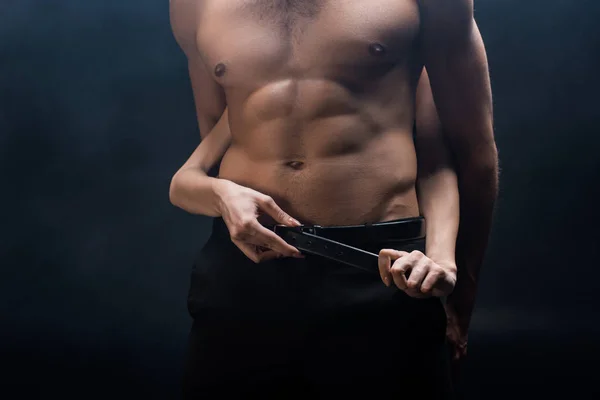 Cropped view of woman taking off belt of shirtless man isolated on black — Stock Photo