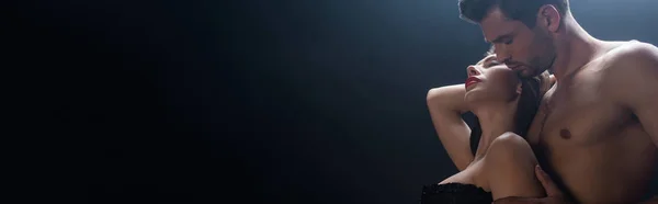 Colpo panoramico di uomo senza maglietta abbracciando donna sexy isolato su nero — Foto stock