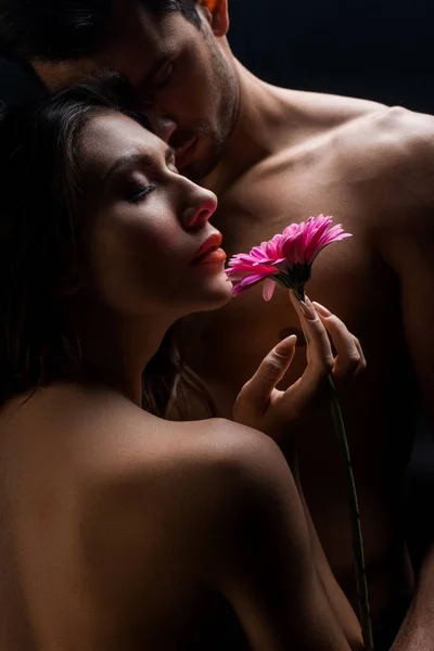 Belle femme nue avec gerbera debout par torse nu petit ami isolé sur noir — Photo de stock