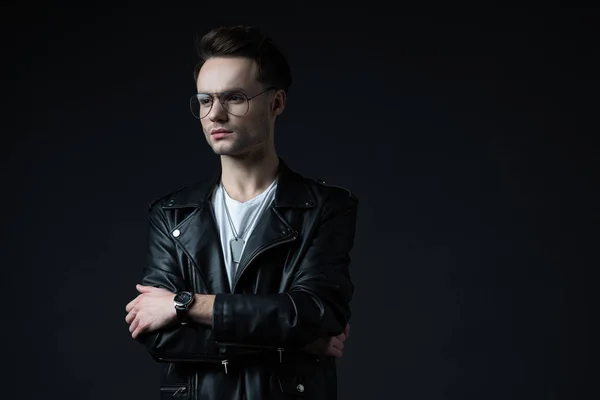 Pensive stylish brutal man in biker jacket looking away with crossed arms isolated on black — Stock Photo