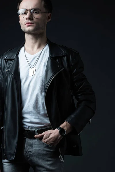 Стильний жорстокий чоловік в куртці для байкерів з рукою в кишені ізольований на чорному — стокове фото