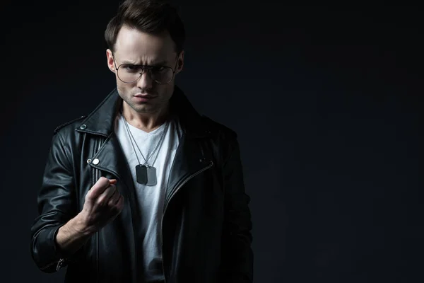 Angry stylish brutal man in biker jacket showing fist isolated on black — Stock Photo