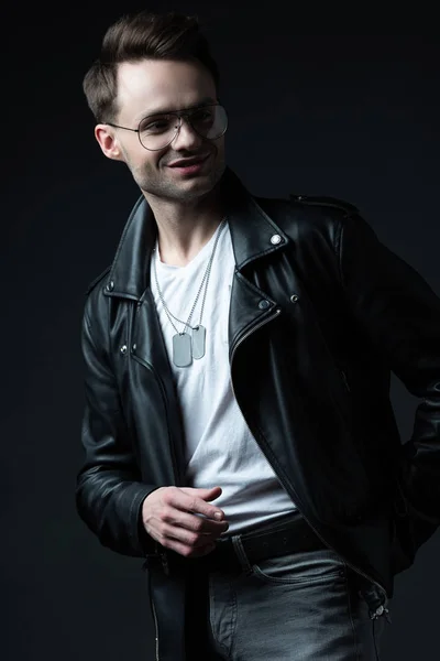 Smiling stylish brutal man in biker jacket pointing with finger aside isolated on black — Stock Photo