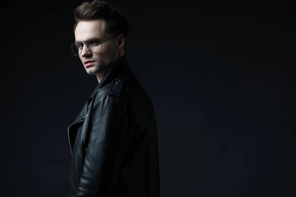 Side view of stylish brutal man in biker jacket looking at camera isolated on black — Stock Photo