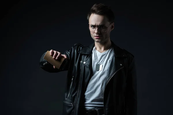 Displeased stylish brutal man in biker jacket pouring out coffee to go isolated on black — Stock Photo