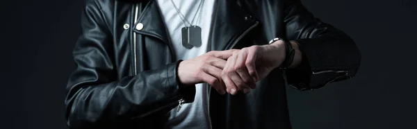 Обрізаний вид стильного жорстокого чоловіка в куртці для байкерів з наручниками ізольовано на чорному, панорамний знімок — стокове фото