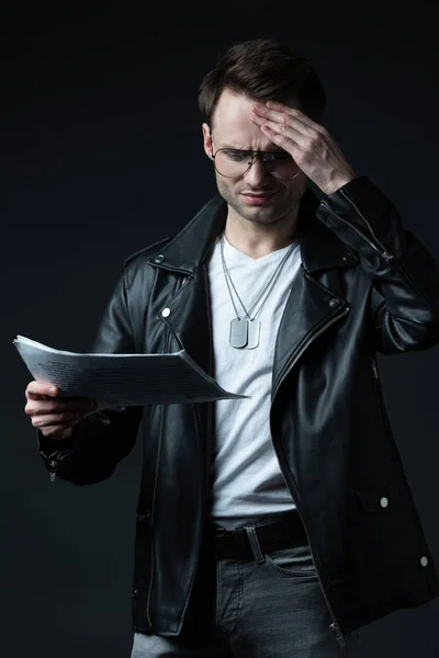 Thoughtful stylish brutal man in biker jacket with newspaper isolated on black — Stock Photo