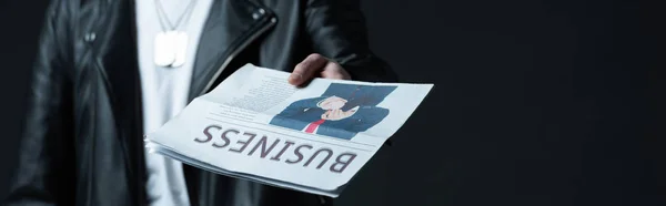 Обрезанный вид стильного жестокого человека в байкерской куртке, показывающий деловую газету, изолированную на черном, панорамный снимок — стоковое фото