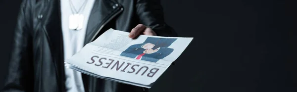 Cropped view of stylish brutal man in biker jacket showing business newspaper isolated on black, panoramic shot — Stock Photo